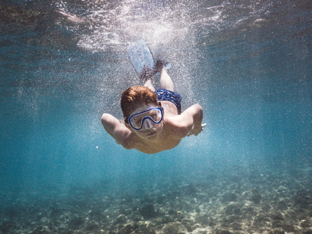 a child wearing snorkel gear dives under the water
