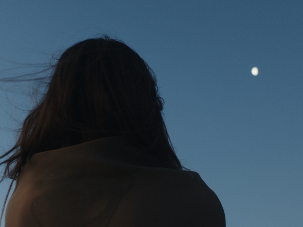 Woman looking up into the sky, with the moon in the distance