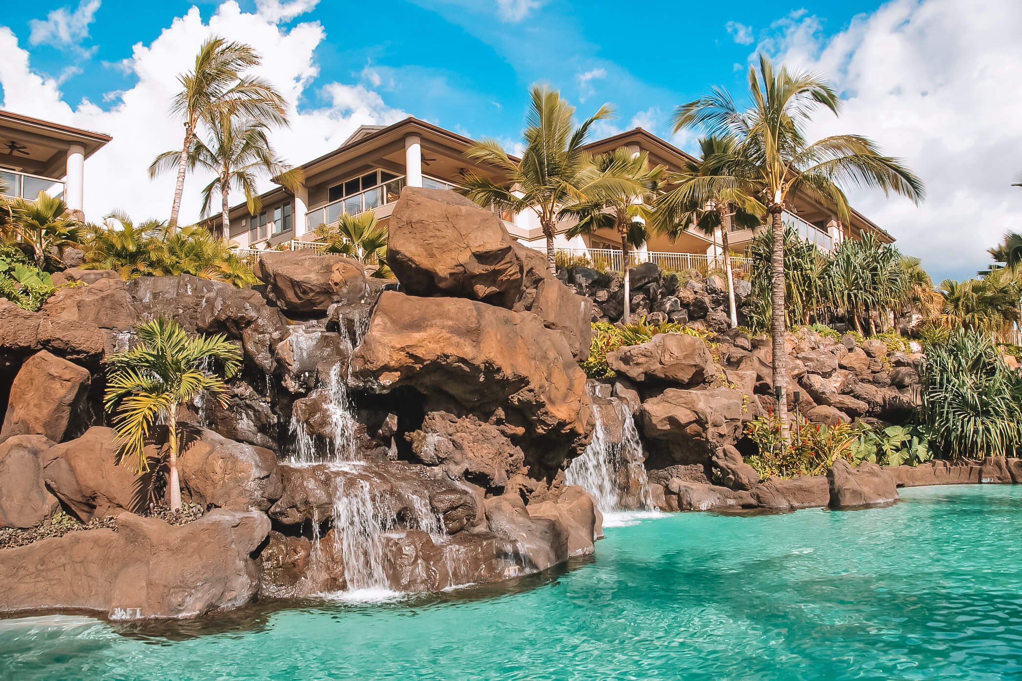 a rock wall with waterfalls drop into a pool in the foreground