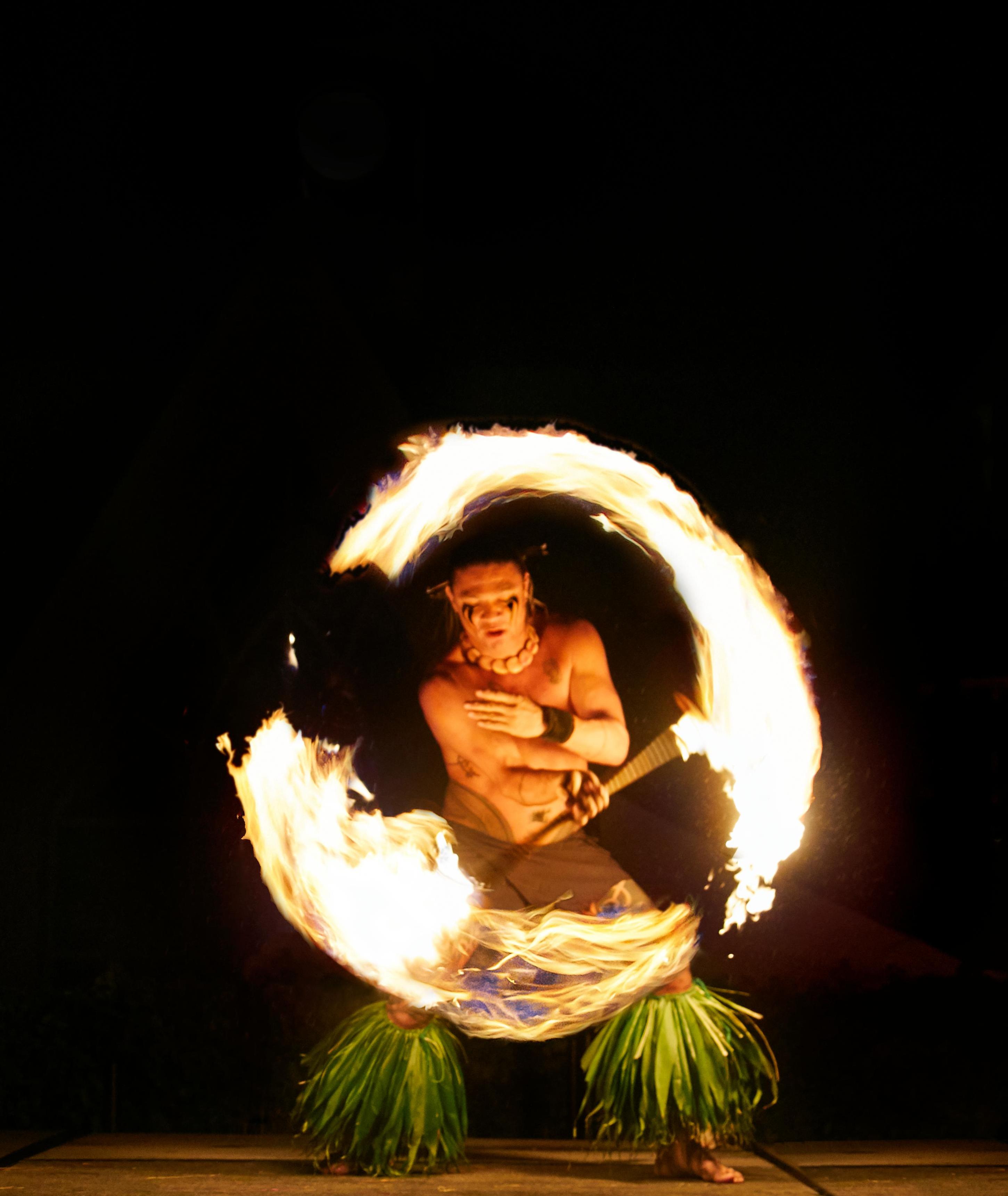 a performer spins fire in a circle in front of a black background