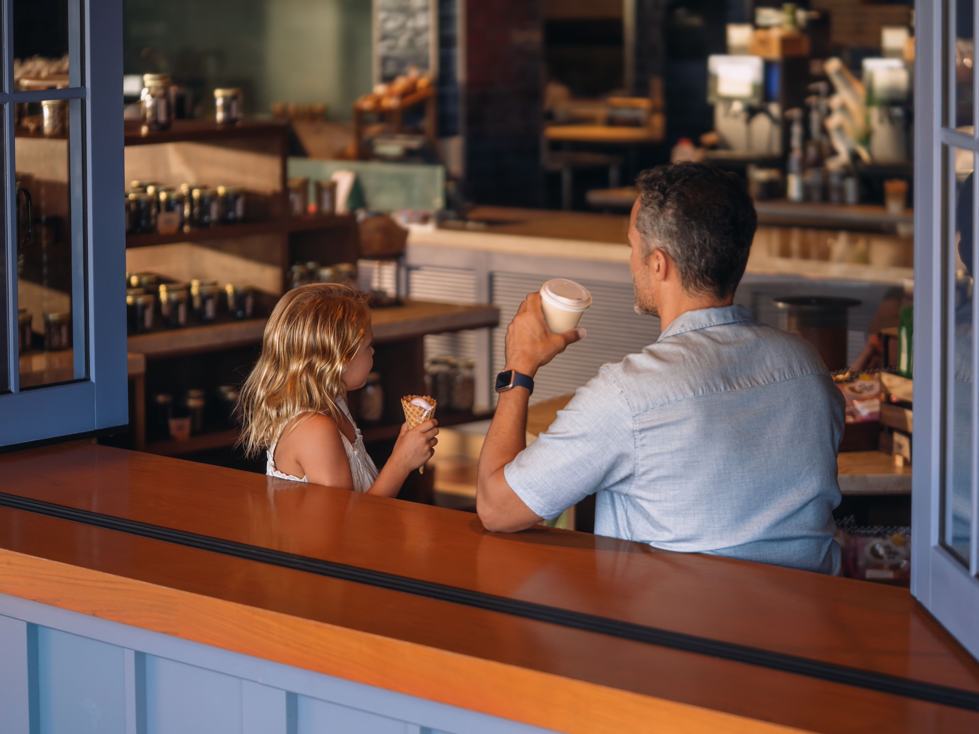 A man enjoys a coffee at a cafe while his daughter eats an ice cream cone