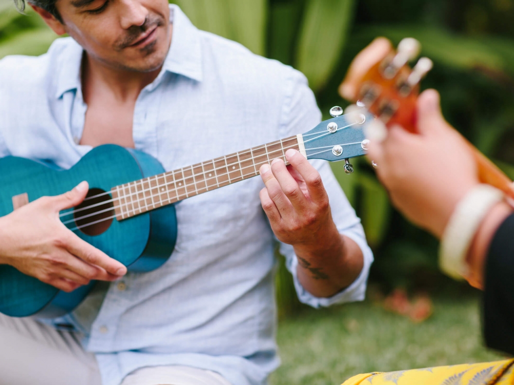 a man holds a blue ukulele while sitting beside a women playing another ukulele