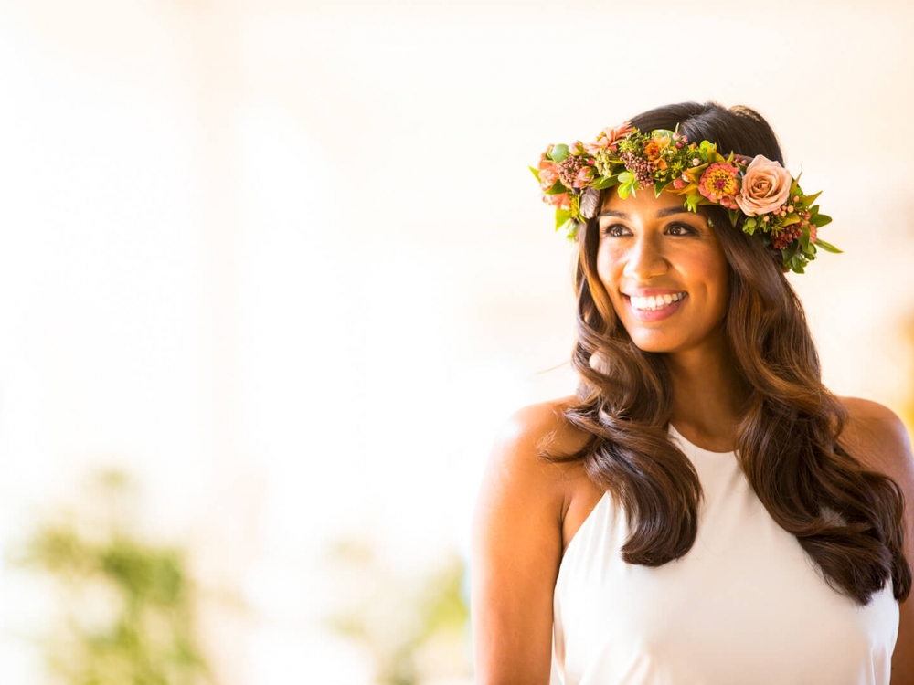 a woman wearing a white top with a flower crown on her head stands in a brightly lit room