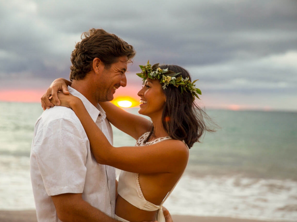 a couple facing each other stand in front of the ocean