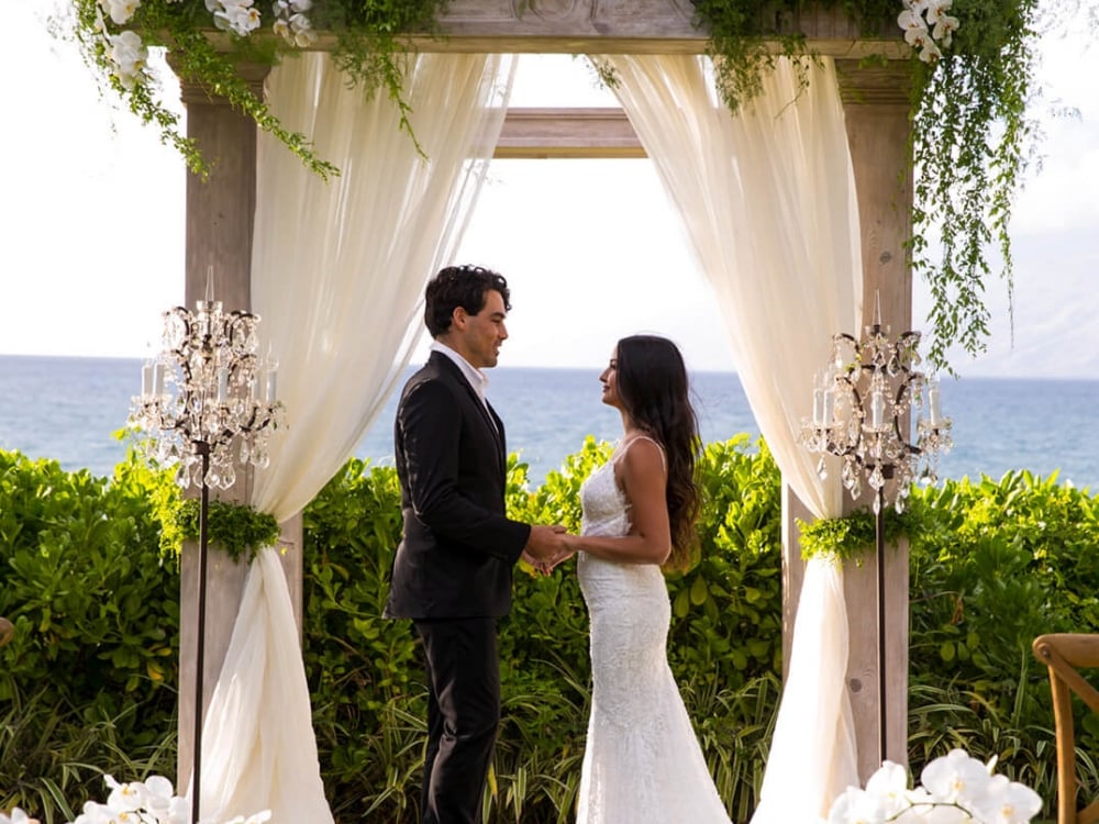 a bride and groom face each other under a pergola decorated with white curtains and white flowers