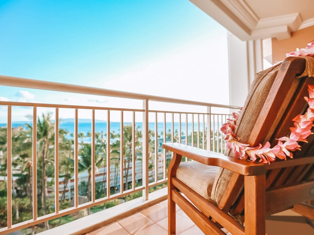 a chair with a pink lei hung from the back sits on a patio overlooking the blue sky and ocean