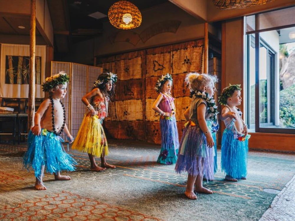 group of children dressed in brightly colored skirts dance 