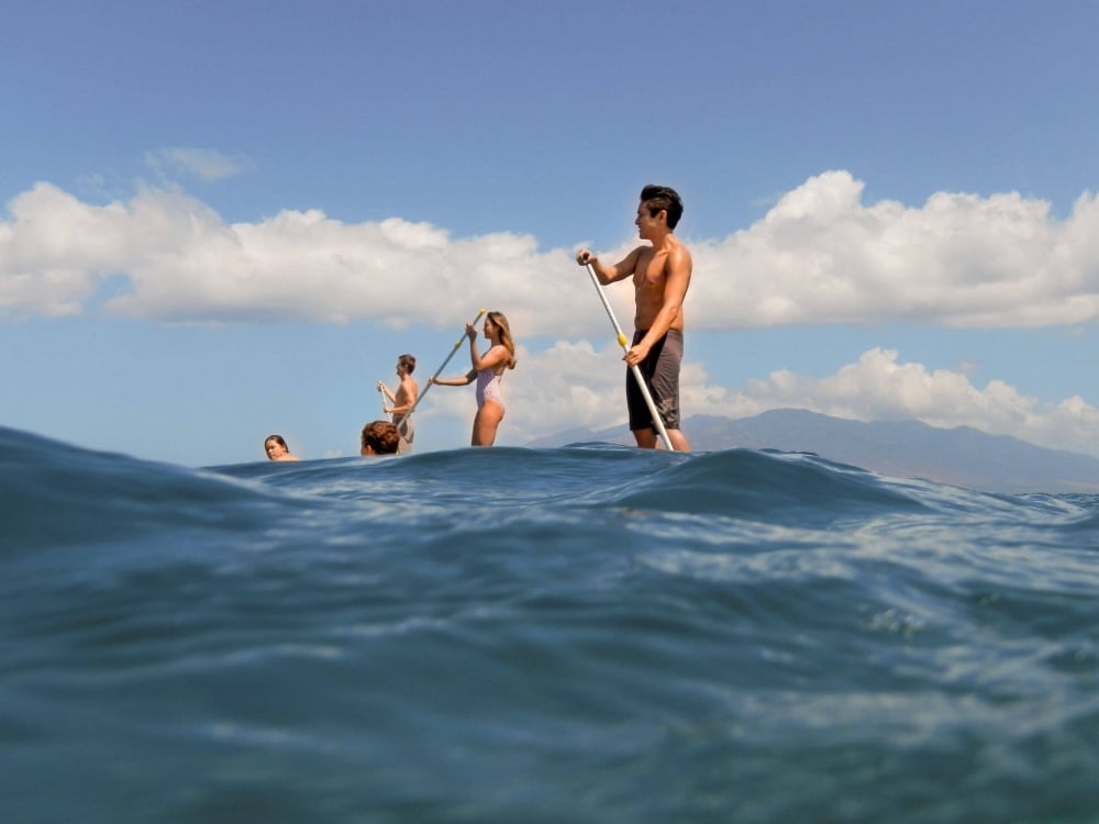 mulitple people on stand up paddle boards in the ocean with blue cloudy sky behind them