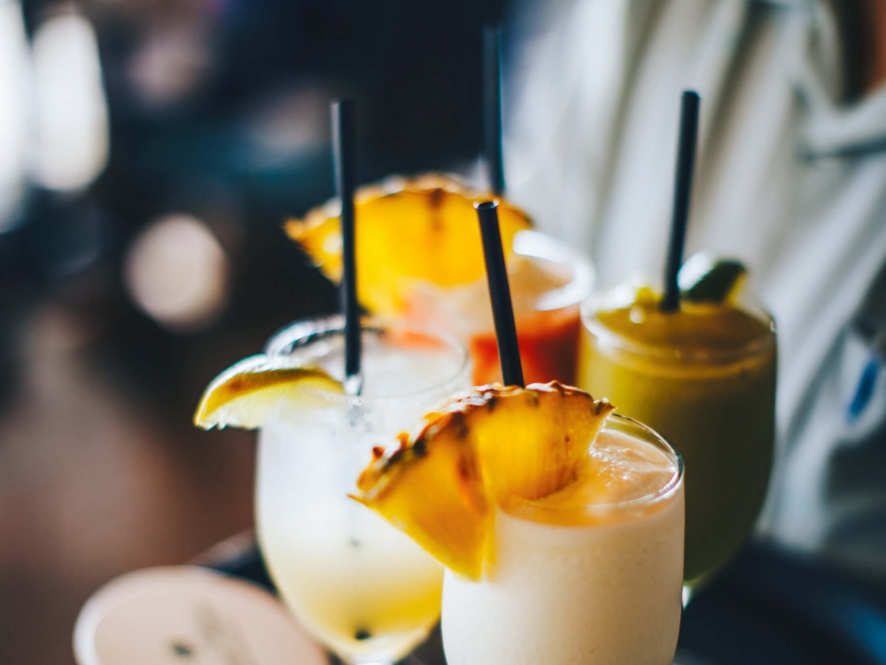 four cocktails held on a black tray by a server in a white collared shirt