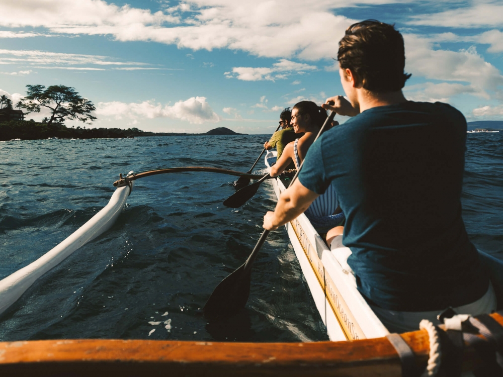 a person in an outrigger canoe against faces the open water below a cloudy sky