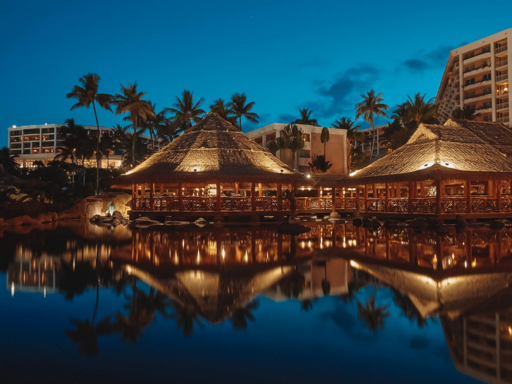 well-lit huts at Grand Wailea restaurant are reflected on the water 