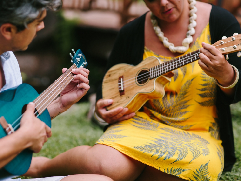 A man and a woman holding brightly colored ukuleles sit on the grass