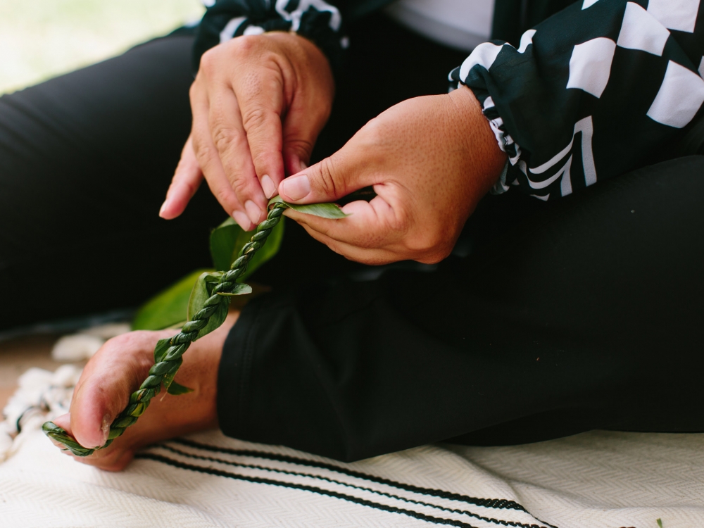 a person weaves a leaf with their hands while holding the base of the weaving with their foot