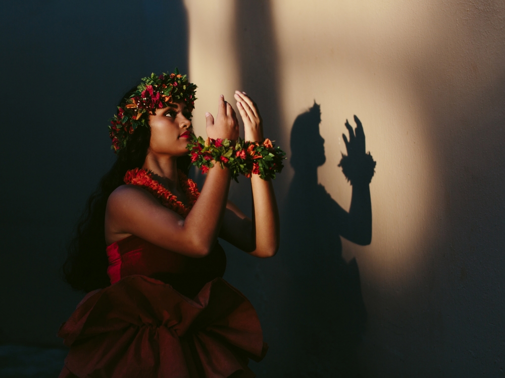 a woman dressed in red dances the luau as the light casts her shadow against the wall beside her