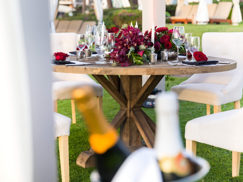 bottles of champage sit in silver bucket in front of a round wooden table covered in flowers and candles