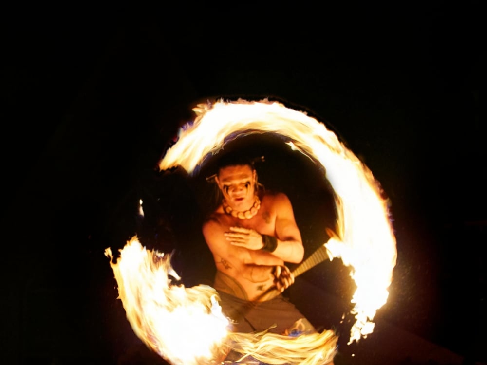 a performer spins fire in a circle in front of a black background