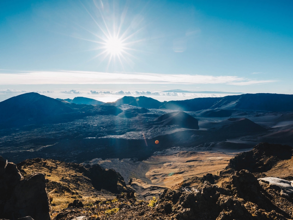 mountainscape with the sun in a cloudless blue sky in the background and valley in the foreground 