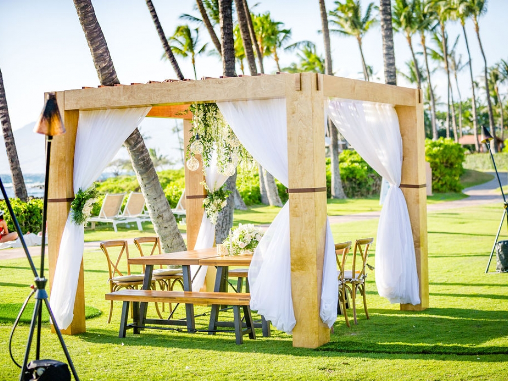 chairs sit around wooden table with white curtains pulled to each corner of pergola stands on the grounds of Grand Wailea resort