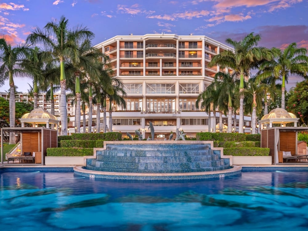 the Grand Wailea resort is framed with palm trees and a large blue water fountain in the foreground
