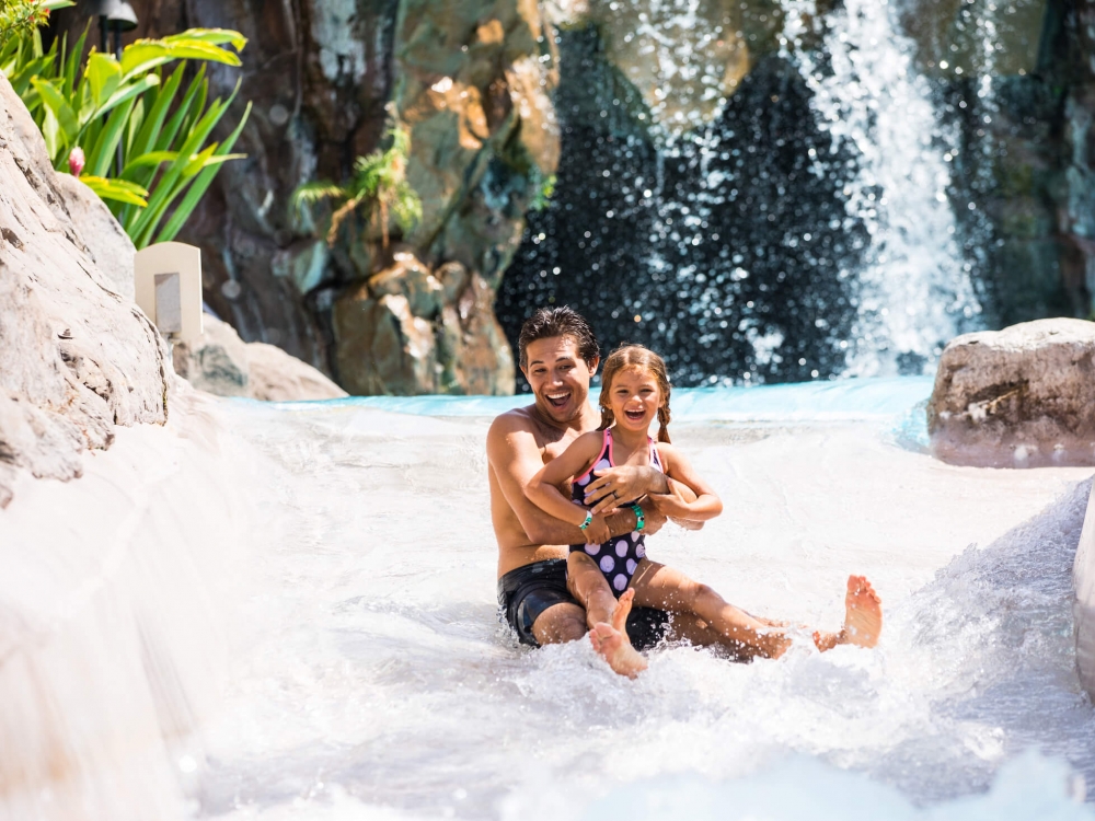 man and child in bathing suits slide down a water slide