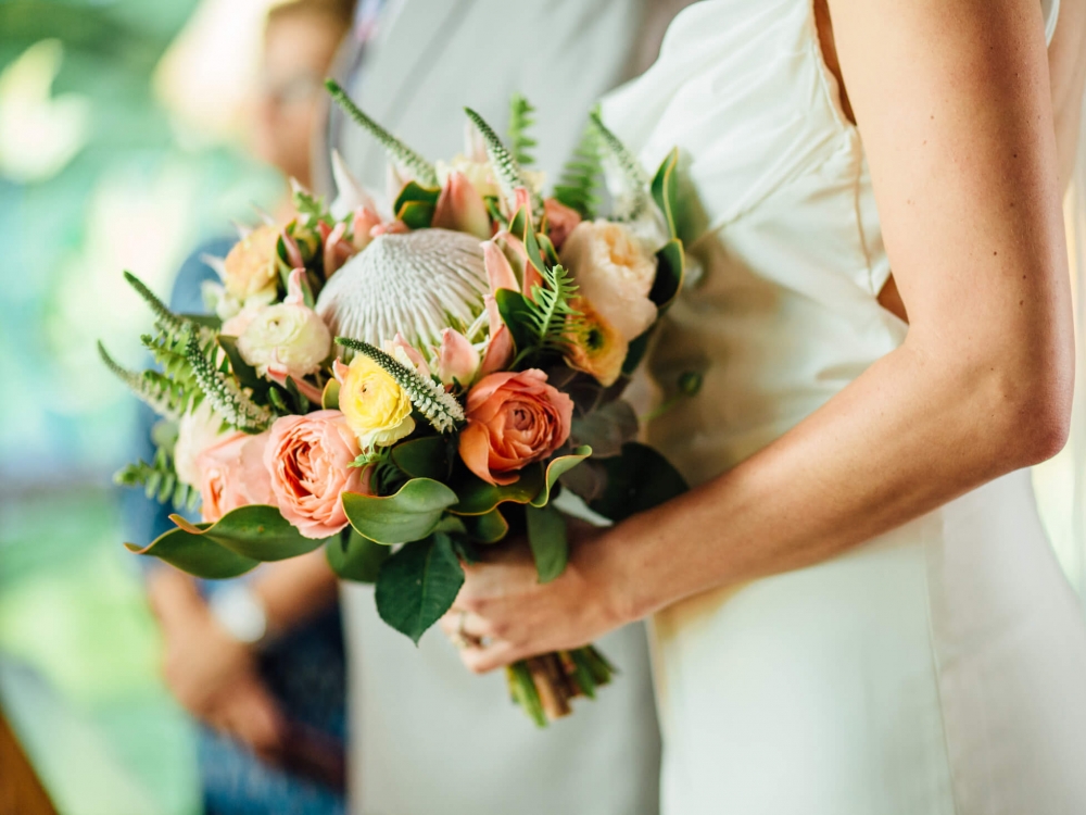 close up of woman in white wedding dress holds bouquet of white flowers in front of her