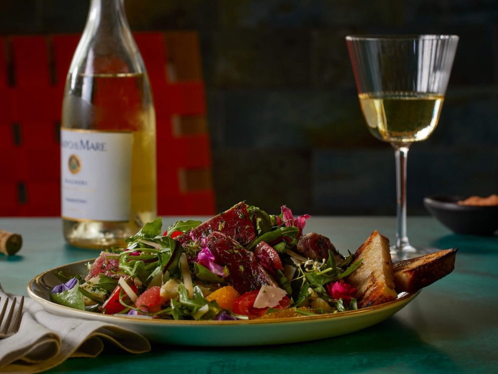 glass of wine with bottle sits behind plate of salad