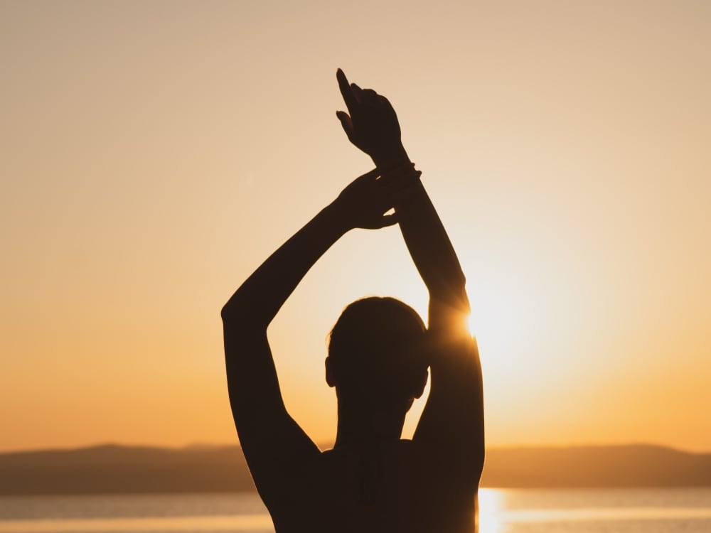 Woman meditating in the setting sun at the waterfront