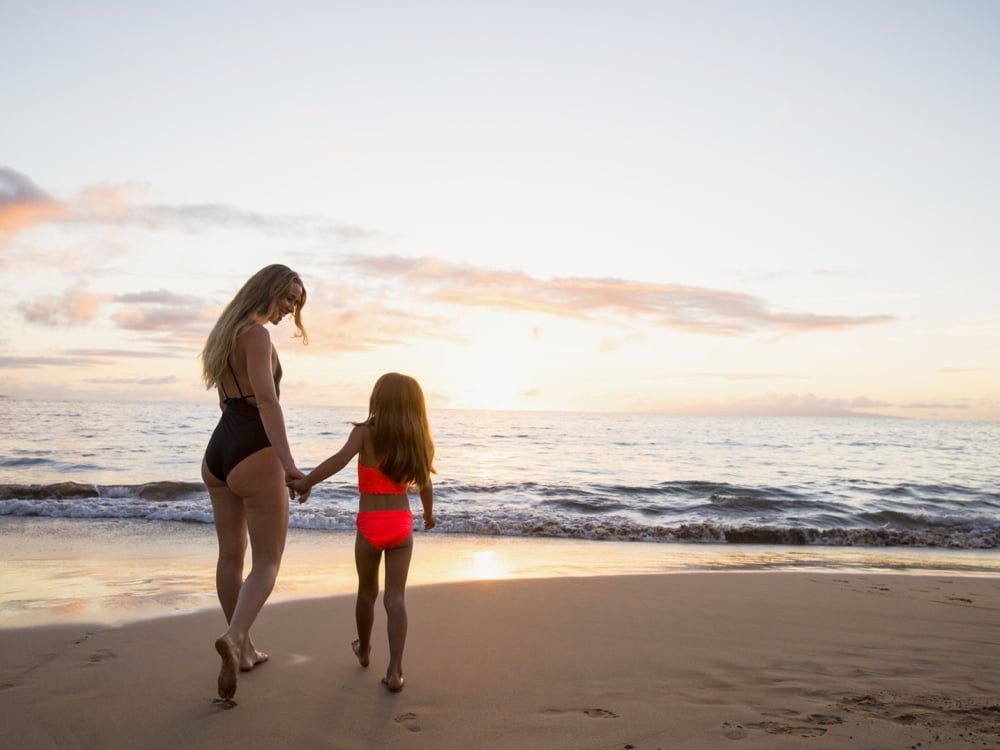 Mother and daughter walk together on beach at sunset