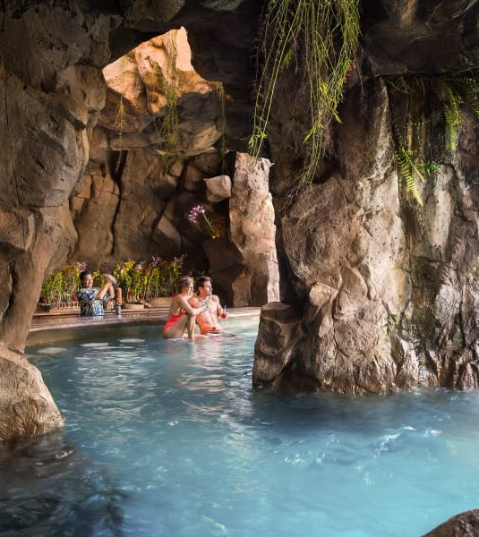 people swim up to grotto bar in a rocky cave while bartender stands behind the bar