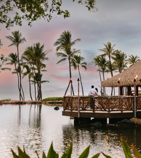 a wooden building overlooks the water lined with palm trees