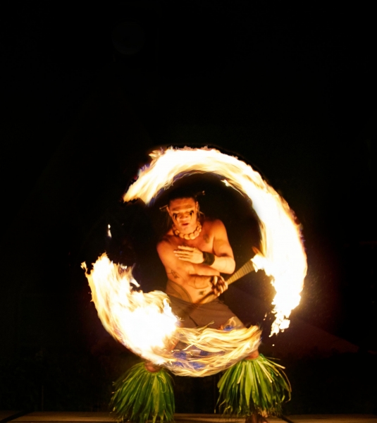 a performer spins fire in a circle in front of a black background