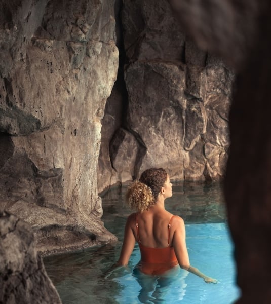 A woman in a bathing suit wades through pristine blue waters in a cave