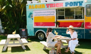 two people sit at a picnic table in front of the Aloha Trick Pony food truck
