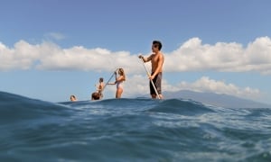 mulitple people on stand up paddle boards in the ocean with blue cloudy sky behind them