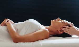woman lays on her back under a white blanked while her head is massaged 