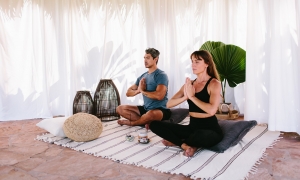 two people sit crosslegged on a striped blanket while meditating