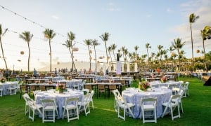 Outdoor banquet with white linen-covered tables under rows of lanterns