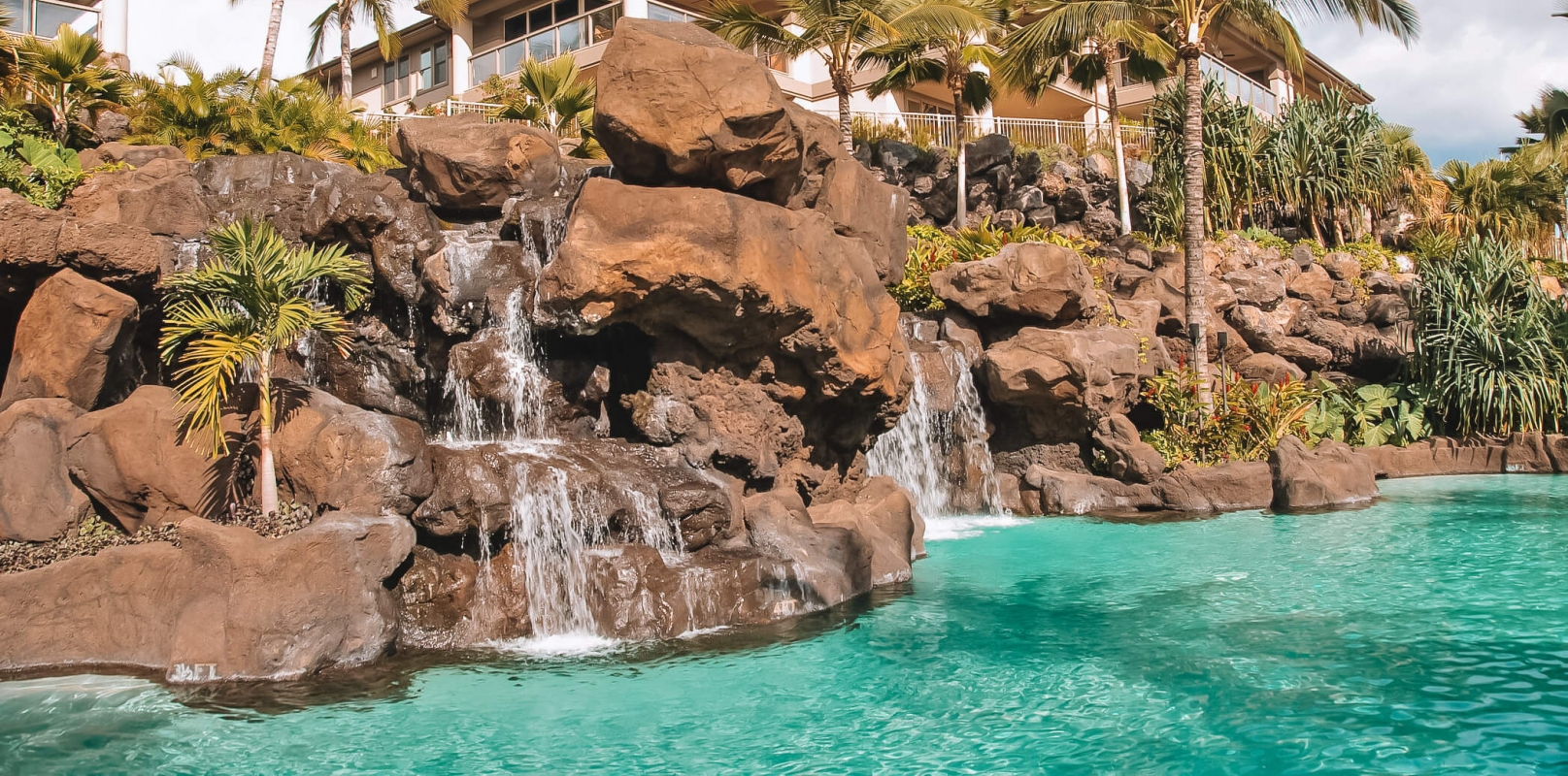 a rock wall with waterfalls drop into a pool in the foreground