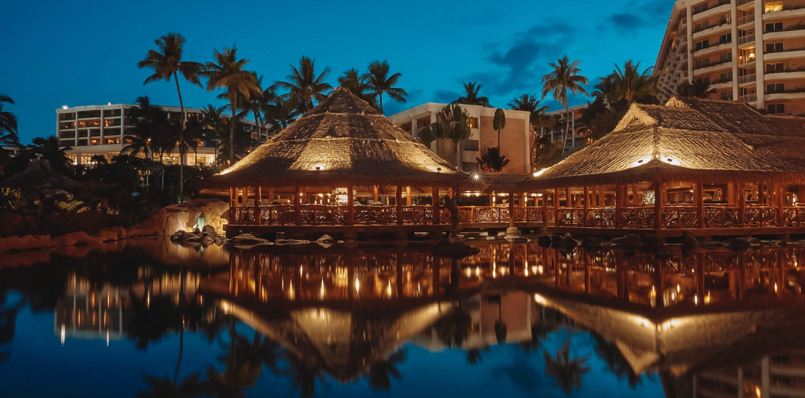 well-lit huts at Grand Wailea restaurant are reflected on the water 