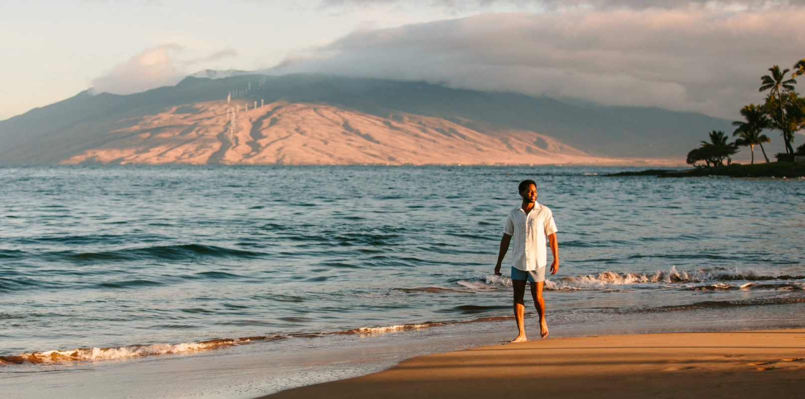 a person walks along the beach beside the ocean with mountains in the background