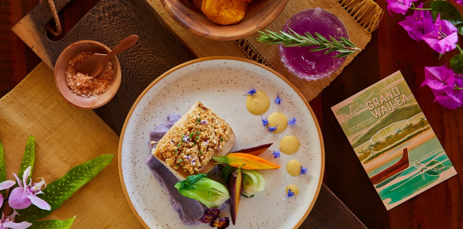flatlay of a plate of fish beside a red cocktail on a wooden table