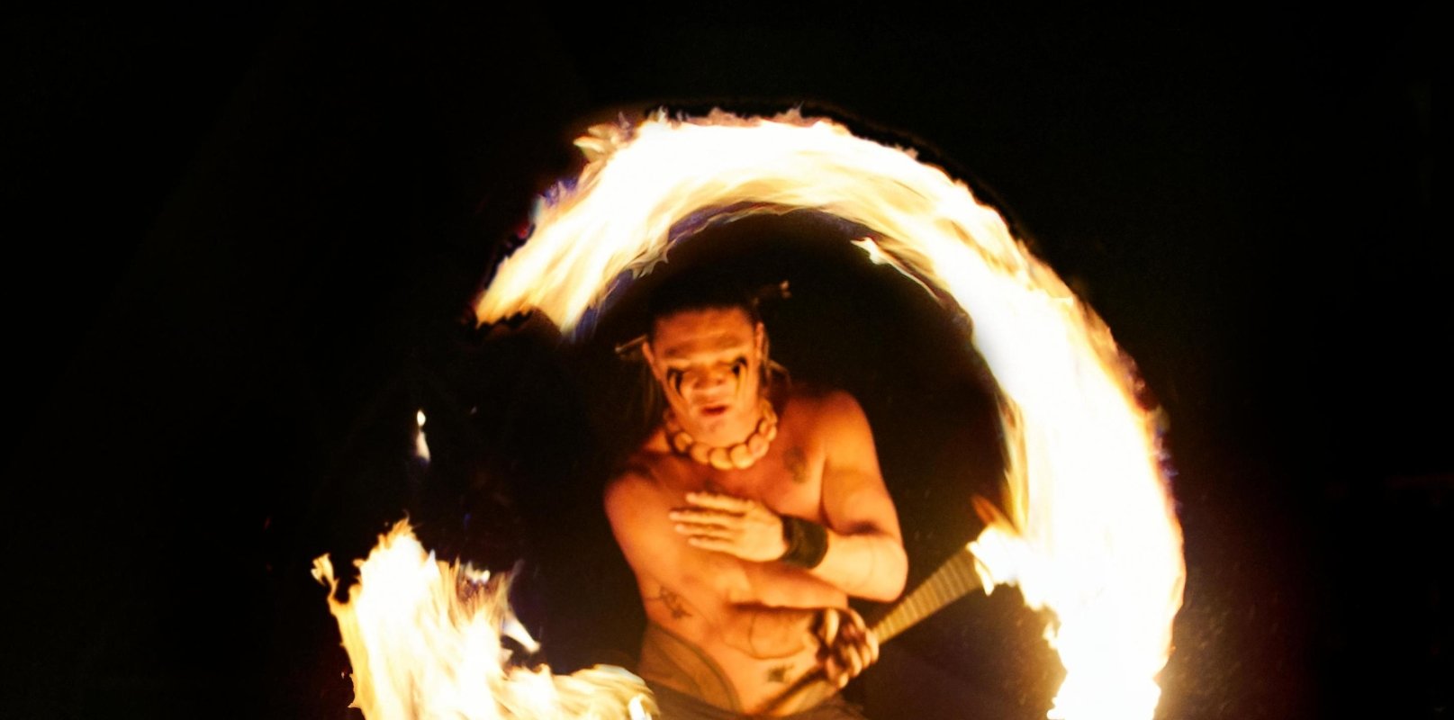 a performer spins fire in a circle in front of a black background