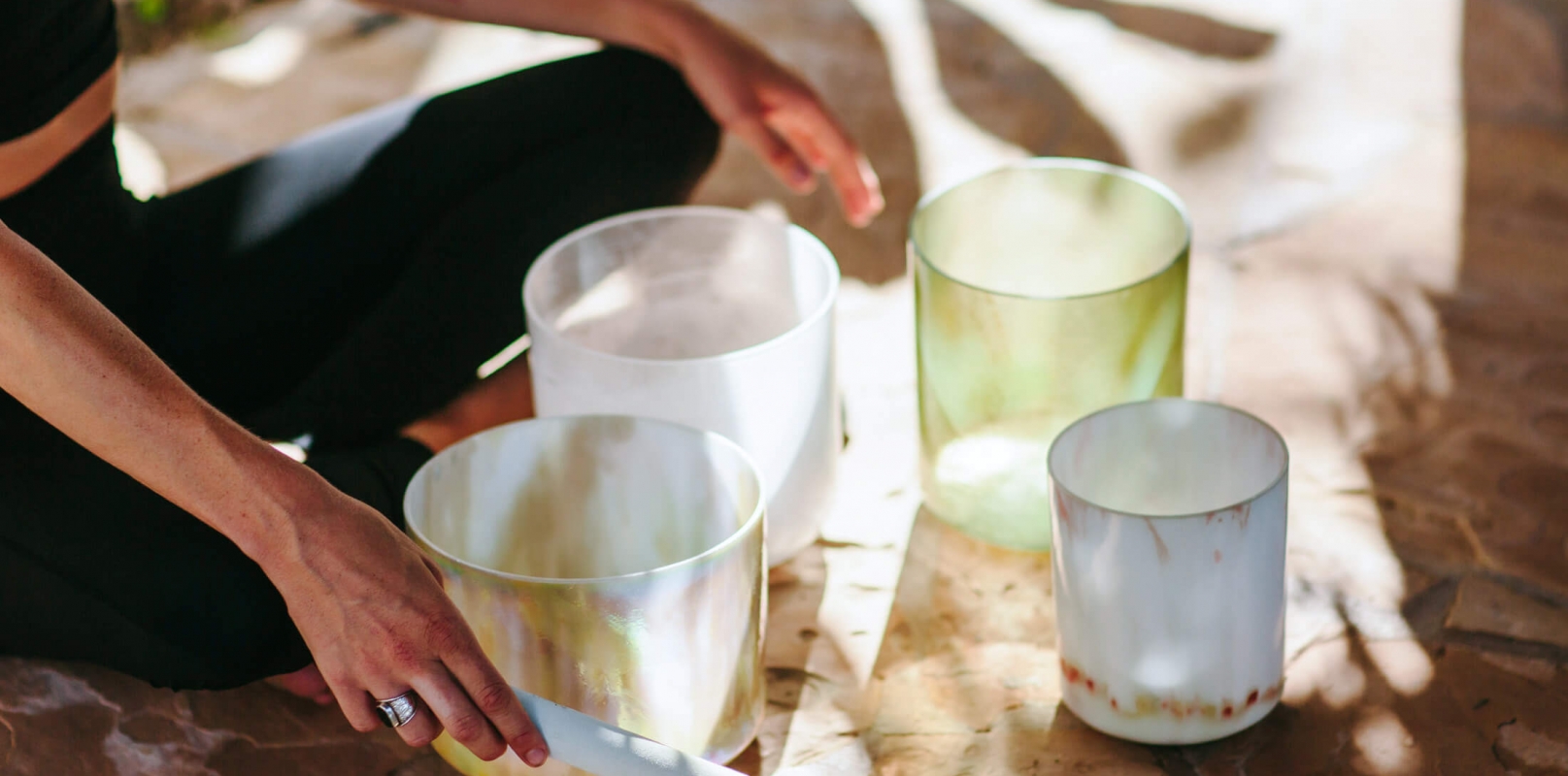 a person sits crosslegged on the ground with multiple sound bowls in front of them