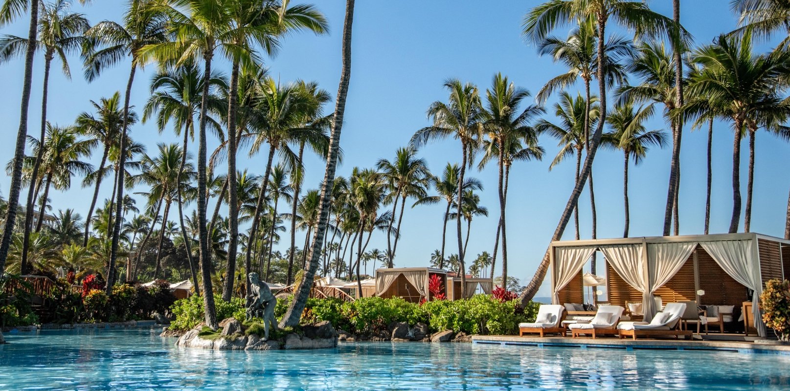 Sun falls on a sparkling blue pool lined with luxury cabanas and waving palm trees