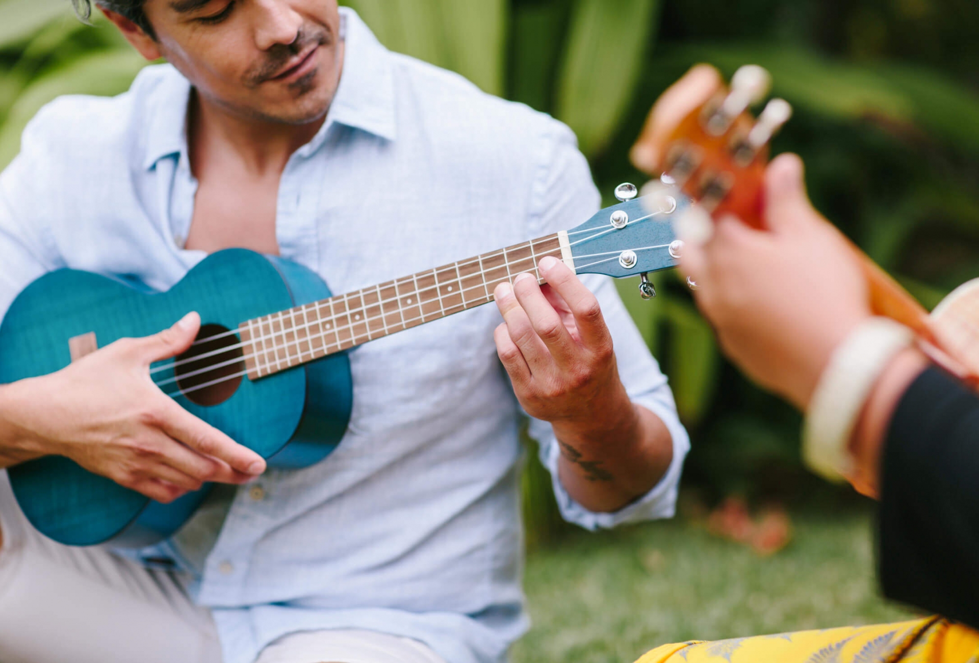 a man holds a blue ukulele while sitting beside a women playing another ukulele
