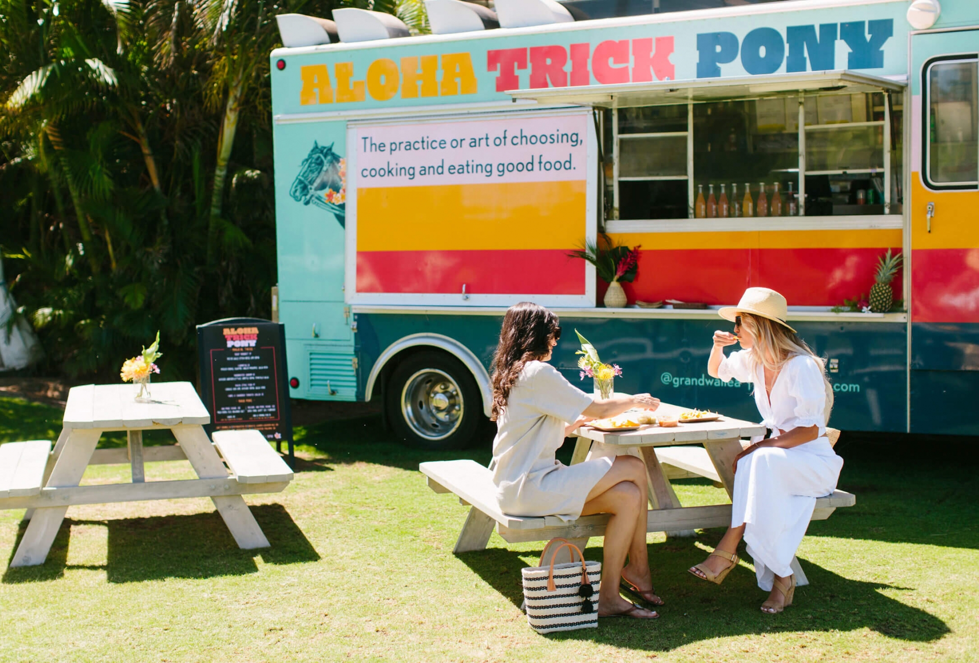 two people sit at a picnic table in front of the Aloha Trick Pony food truck