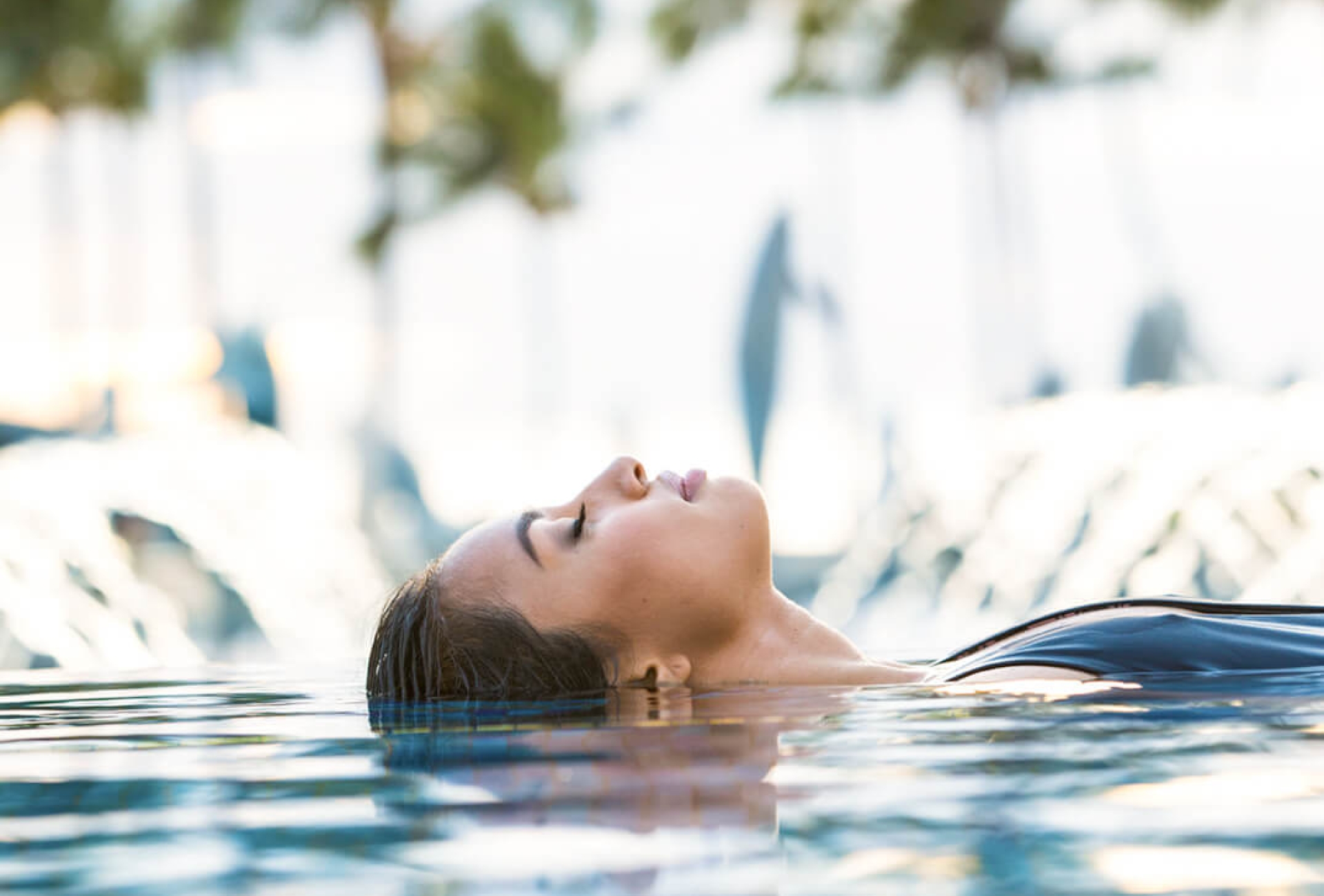 woman in pool floats on her back with palm trees in the background