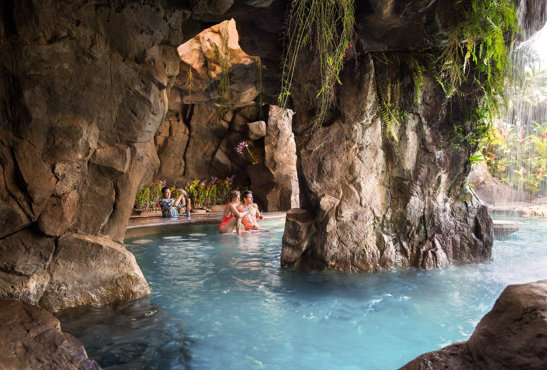 people swim up to grotto bar in a rocky cave while bartender stands behind the bar