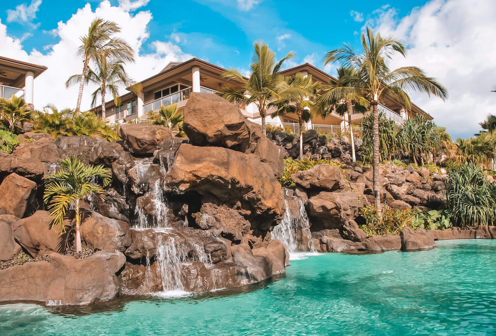 a rock wall with waterfalls drop into a pool in the foreground