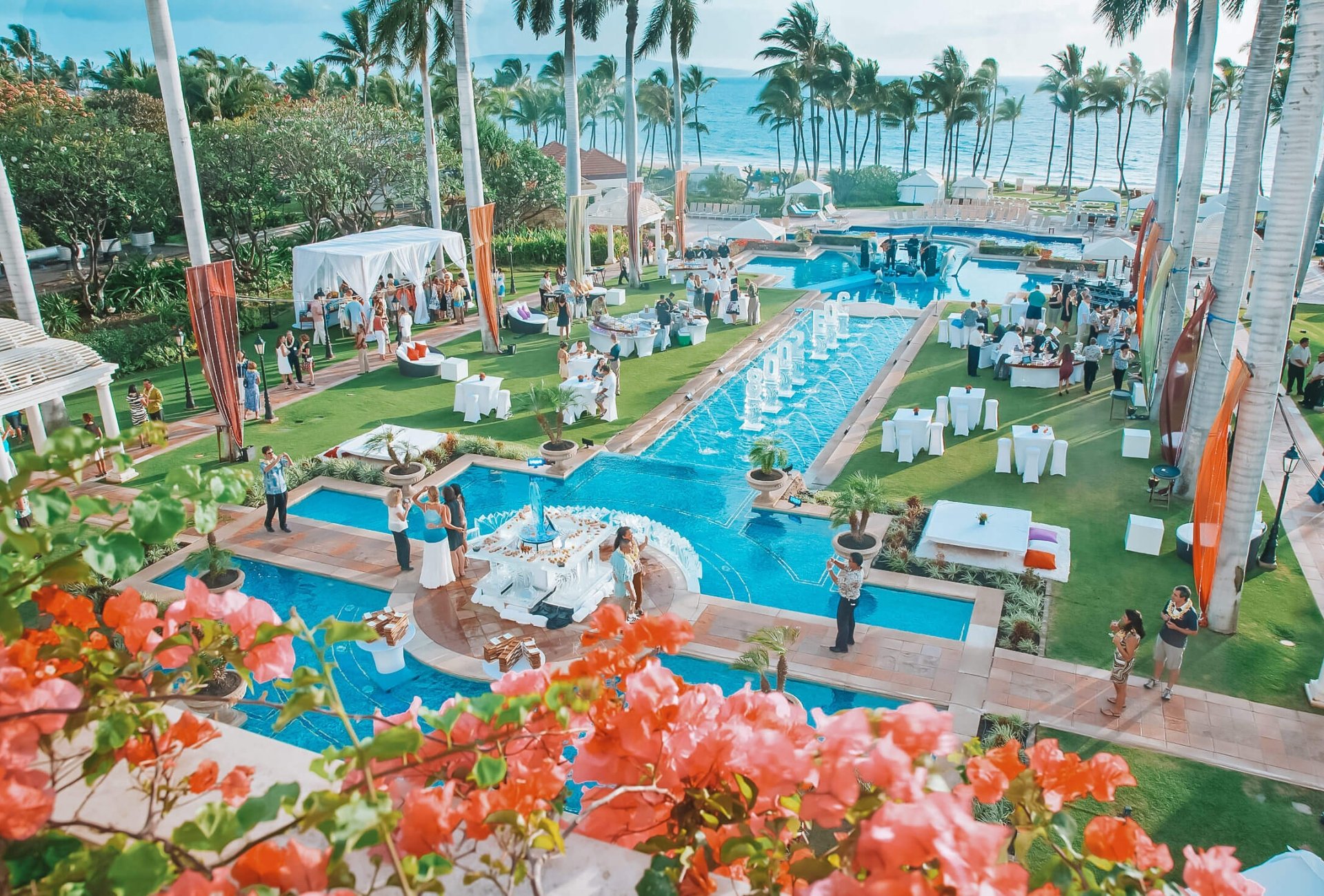 a water feature with multiple levels pours water into a larger pool with palm trees in the background